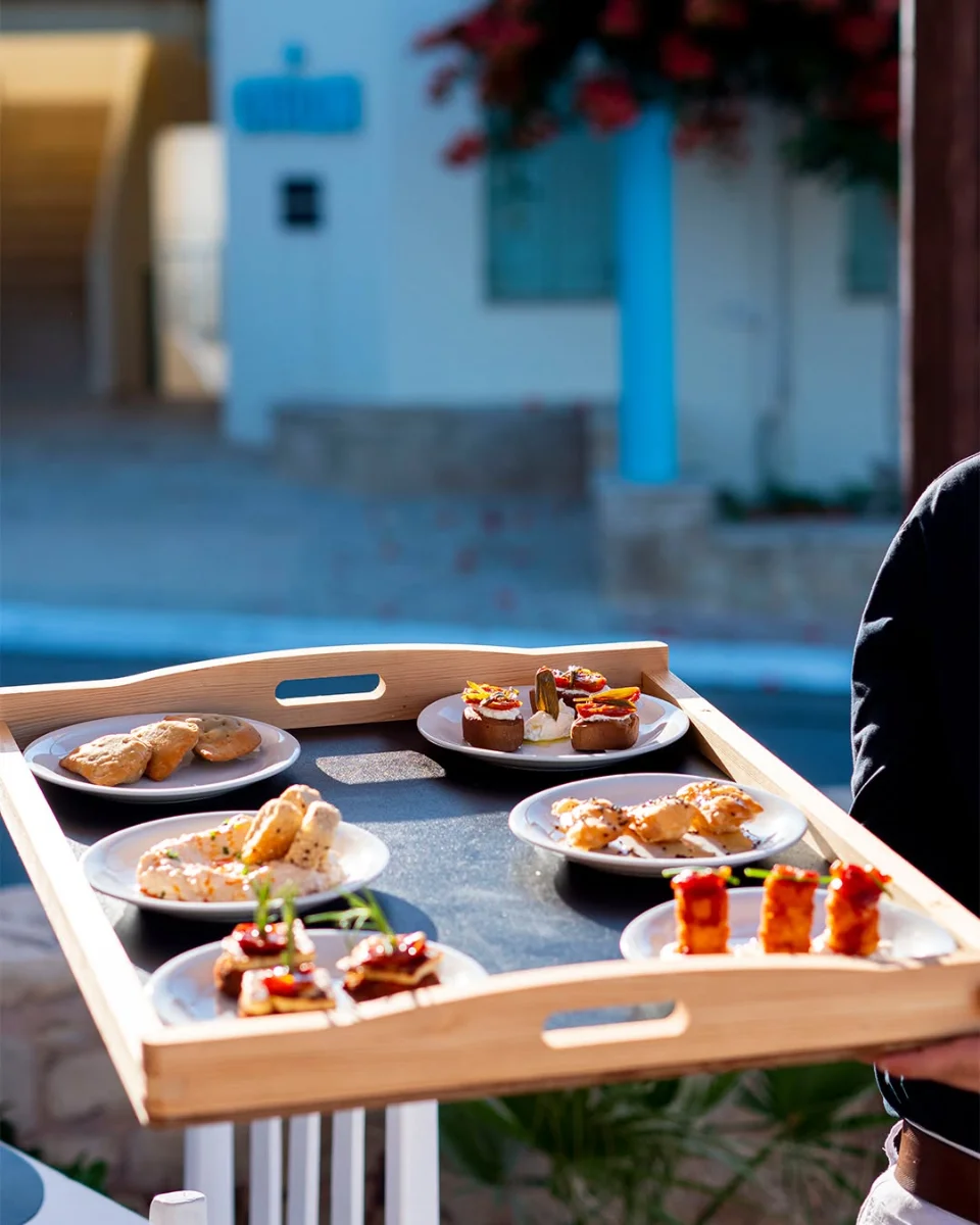 A waiter carrying a wooden tray of meze plates across the terrace